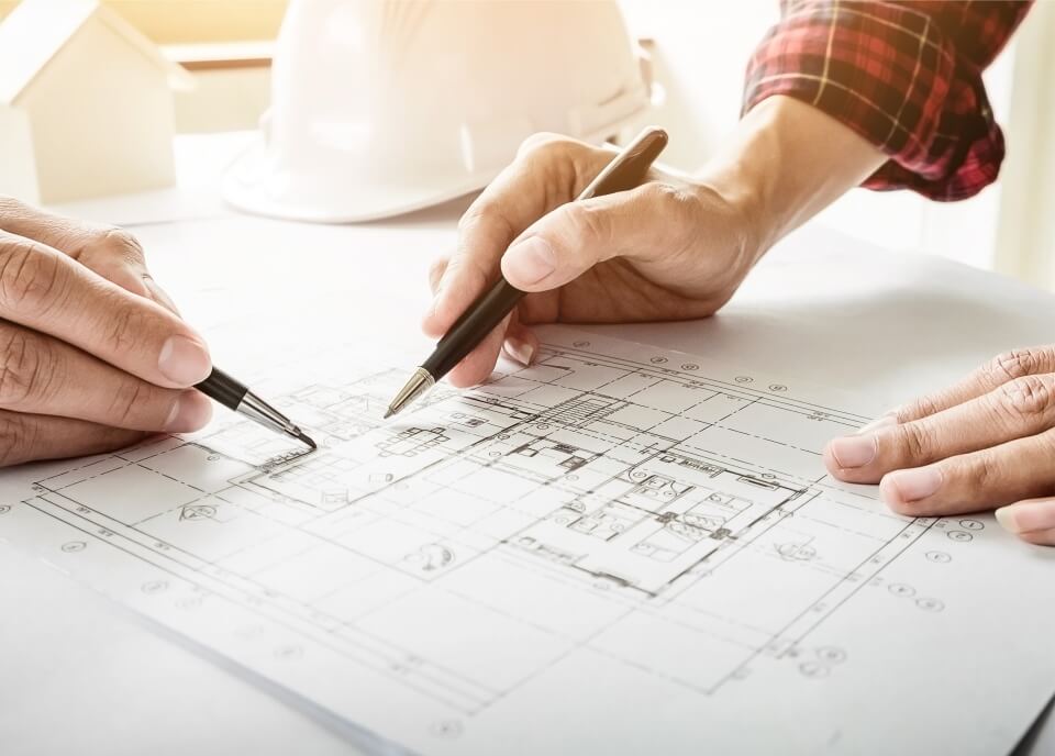 Two people are holding pens and going through construction drawings