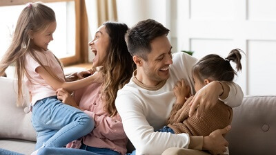 Dad mom and two girls laughing in the living room of the house